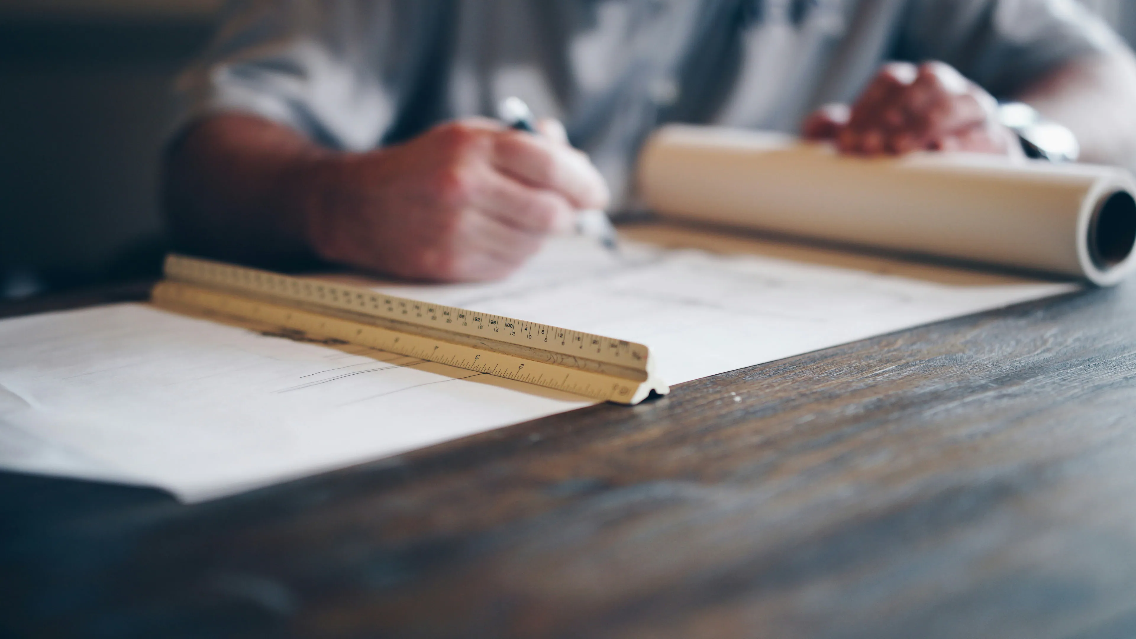 Main traçant au crayon sur un plan avec une règle d'échelle